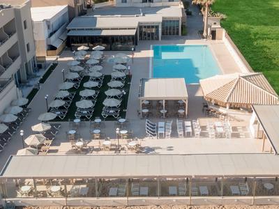 Hotelterrasse mit Pool, Tischen und Sonnenschirmen, angrenzend an eine Grünfläche.