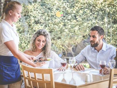 Pár sedí u stolu a servírka jim v restauraci servíruje jídlo.