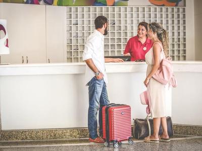 Muž a žena s kufrem mluví s recepční u hotelové recepce.