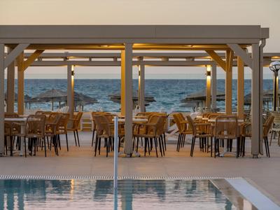 Überdachter Sitzbereich mit Holzmöbeln neben einem Pool und Blick aufs Meer.