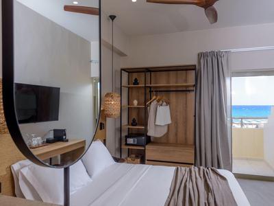 Moderní hotelový pokoj s manželskou postelí, velkým zrcadlem, otevřenou skříní a výhledem na moře z balkonu