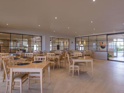 Heller, moderner Speisesaal mit Holzstühlen und Tischen, großen Fenstern und minimalistischer Einrichtung.