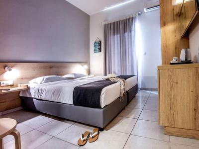 Moderní hotelový pokoj s manželskou postelí, nočními stolky, televizí a závěsy na okně.