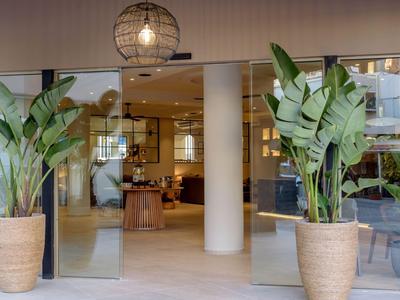Moderner Hoteleingang mit großen Pflanzen in Töpfen und einem beleuchteten Innenraum.