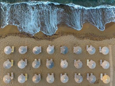 Vue aérienne de la plage avec des parasols blancs et des vagues arrivantes.