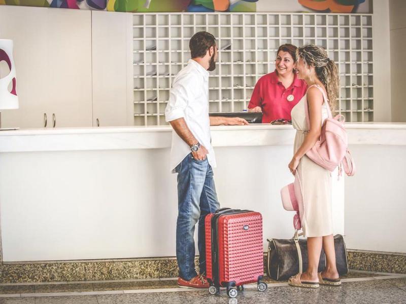 Muž a žena s kufrem mluví s recepční u hotelové recepce.