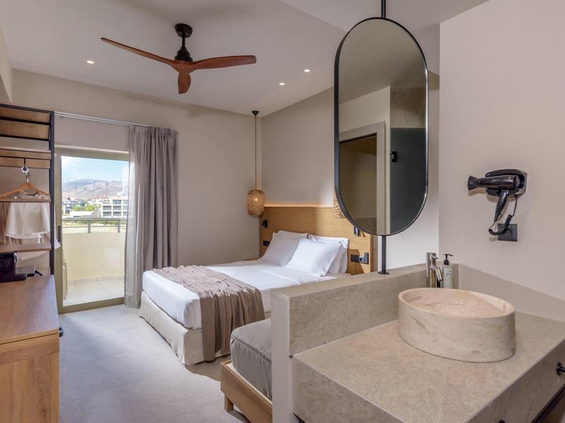 Moderní hotelový pokoj s manželskou postelí, velkým zrcadlem a balkonem s výhledem.