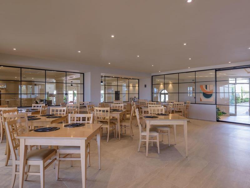 Světlá moderní kavárna s dřevěnými židlemi a stoly, velkými okny a minimalistickým designem.