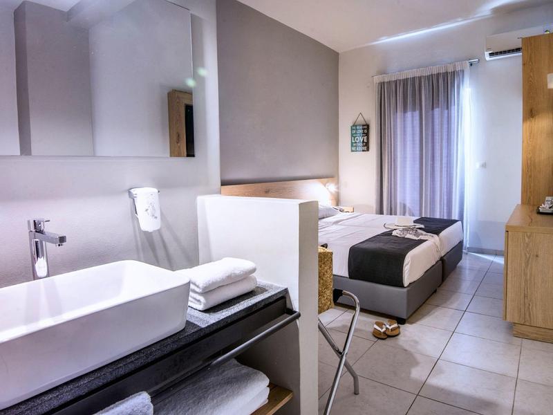 Moderní hotelový pokoj s jednolůžkem, umyvadlem v pokoji a světlým dřevěným nábytkem.