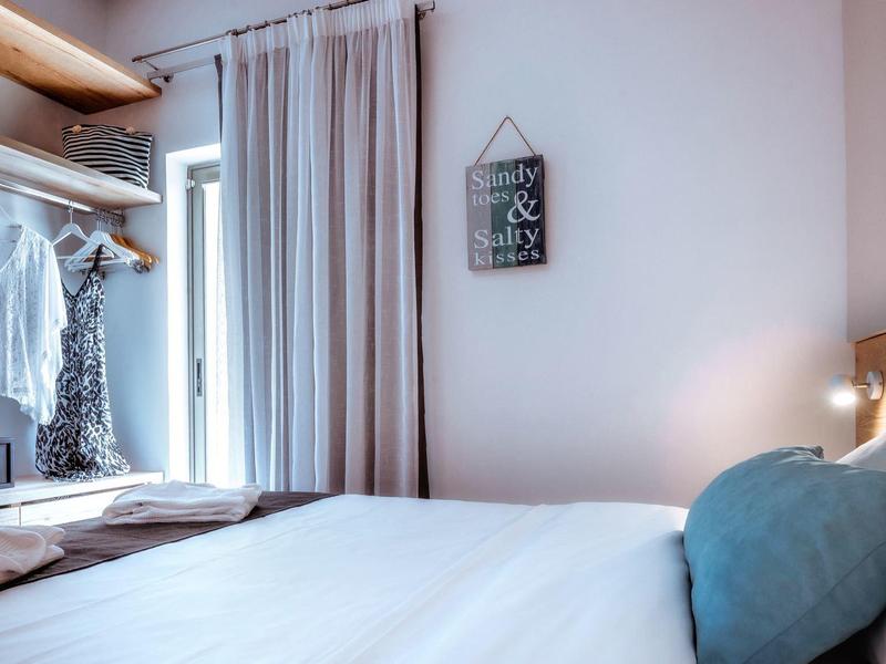 Světlá, útulná ložnice s velkou postelí, závěsy a skříní.