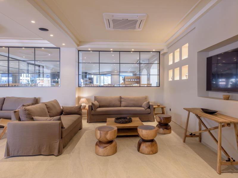 Moderní hotelová lounge s pohovkami, dřevěnými stoličkami a velkou televizí.