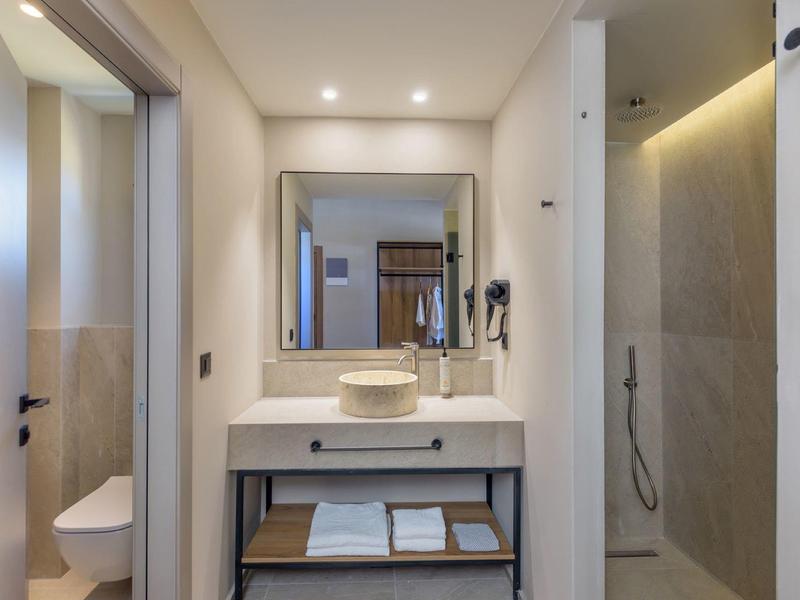 Moderní hotelová koupelna se zrcadlem, umyvadlem, ručníky a sprchou.