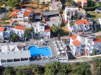 Luchtfoto van een resort met witte gebouwen, zwembaden en omliggend groen.