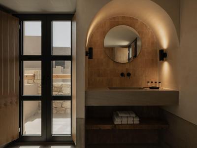 Moderne badkamer met ronde spiegel, stenen muur en raam dat natuurlijk licht binnenlaat.