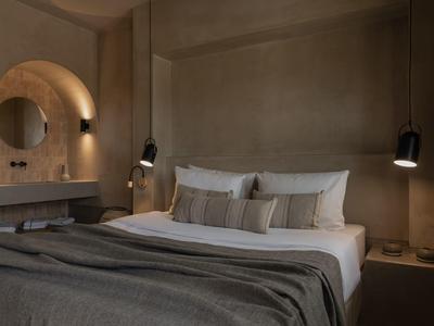 Modern hotelkamer met groot bed, grijze beddengoed en minimalistische verlichting.