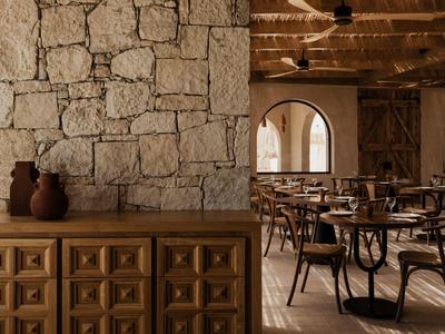 Rustiek restaurant met stenen muur, houten meubels en gedekte tafels in warm licht.