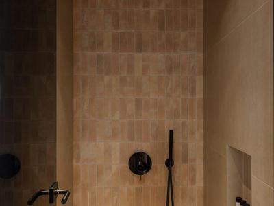 Moderne douche met beige tegels, zwarte douchekop en muurnis.