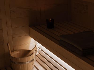 Sauna z drewnianą ławką, drewnianym wiadrem i delikatnym oświetleniem pod ławką