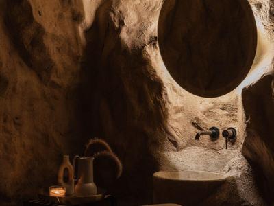 Rustykalna łazienka z okrągłym lustrem i światłem świecy w kamiennej wnęce.