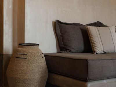 Elegante zithoek met donkere kussens en een grote geweven mand naast een houten voet.