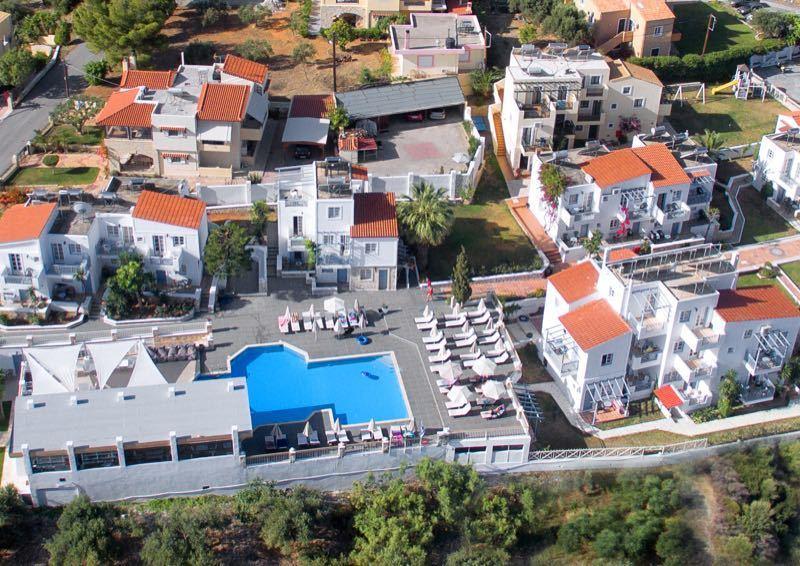 Luchtfoto van een resort met witte gebouwen, zwembaden en omliggend groen.
