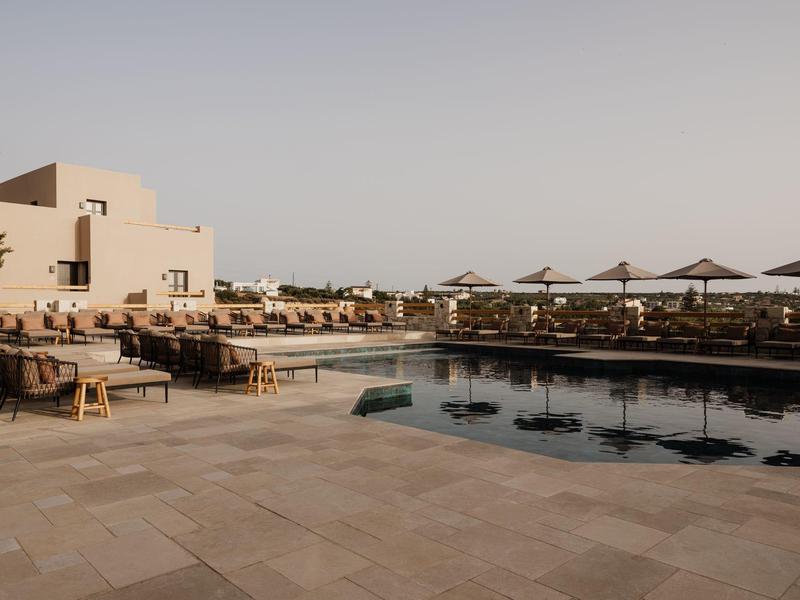 Buitenzwembad met ligstoelen en parasols bij modern hotelgebouw onder heldere hemel.
