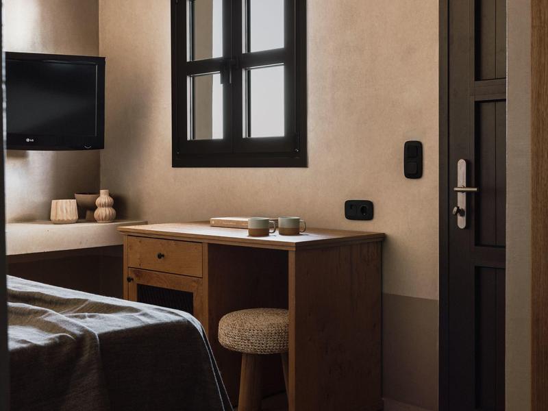 Gezellige hotelkamer met bureau, tv en raam waar warm licht binnenvalt.