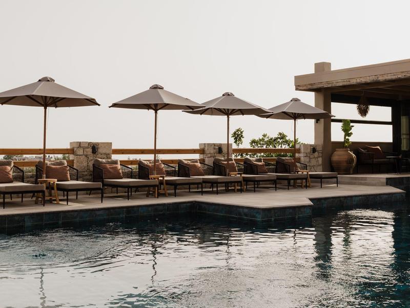 Buitenzwembad met ligbedden en parasols naast het water onder een heldere lucht.