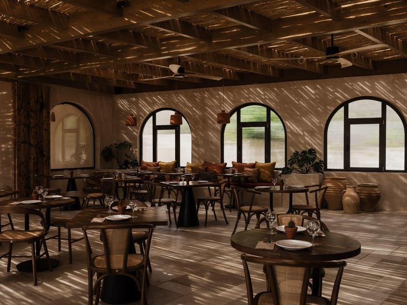 Rustiek restaurant met houten tafels en stoelen, boogvormige ramen en zonlicht dat schaduwen werpt.