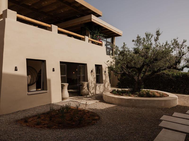 Moderne beige villa met terras en weelderige tuin onder zacht zonlicht.