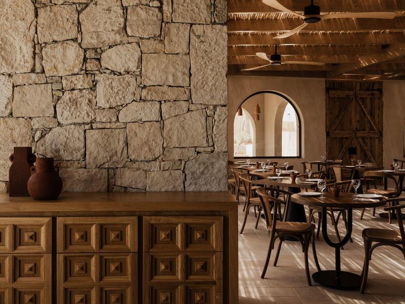 Rustiek restaurant met stenen muur, houten meubels en gedekte tafels in warm licht.