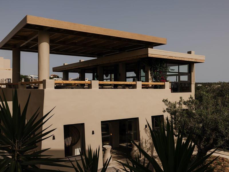 Moderne beige villa met grote ramen en ruim open dakterras omringd door groen.