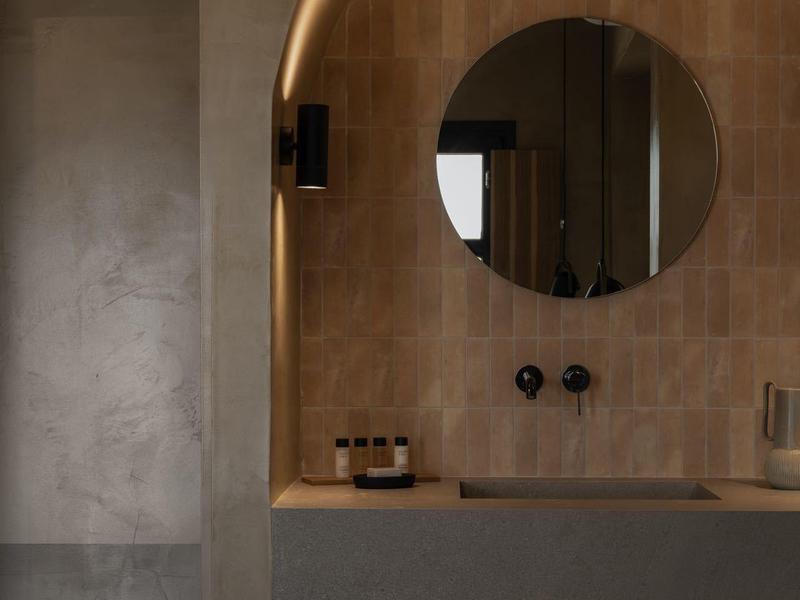 Moderne badkamer met ronde spiegel, wastafel en netjes gestapelde handdoeken onder de gootsteen.