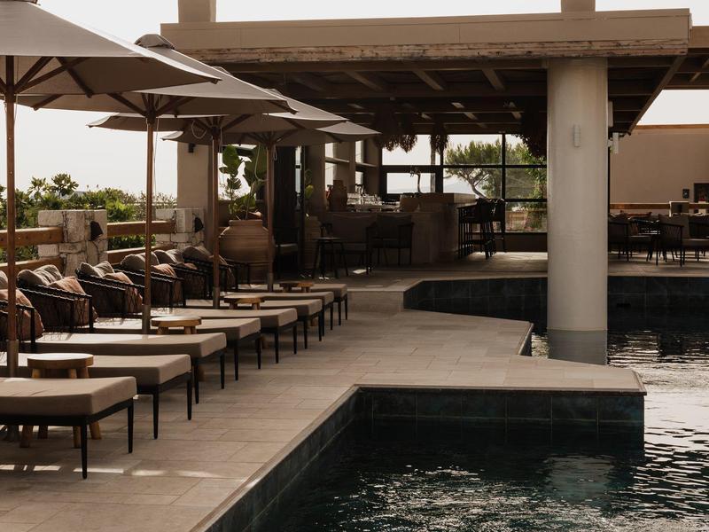 Buitenzwembad met ligstoelen en grote parasols onder een houten pergola.