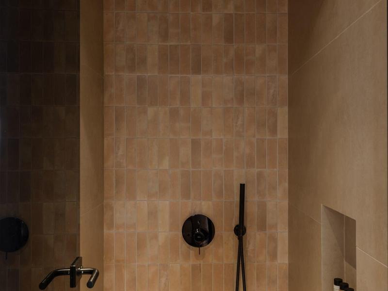 Moderne douche met beige tegels, zwarte douchekop en muurnis.