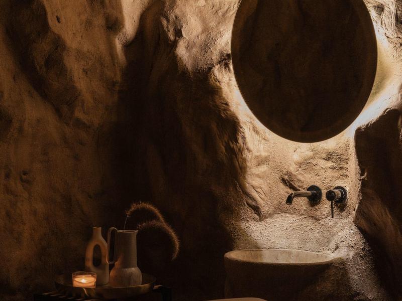 Rustieke badkamer met ronde spiegel, wastafel en handgemaakt materiaal in grotwand.