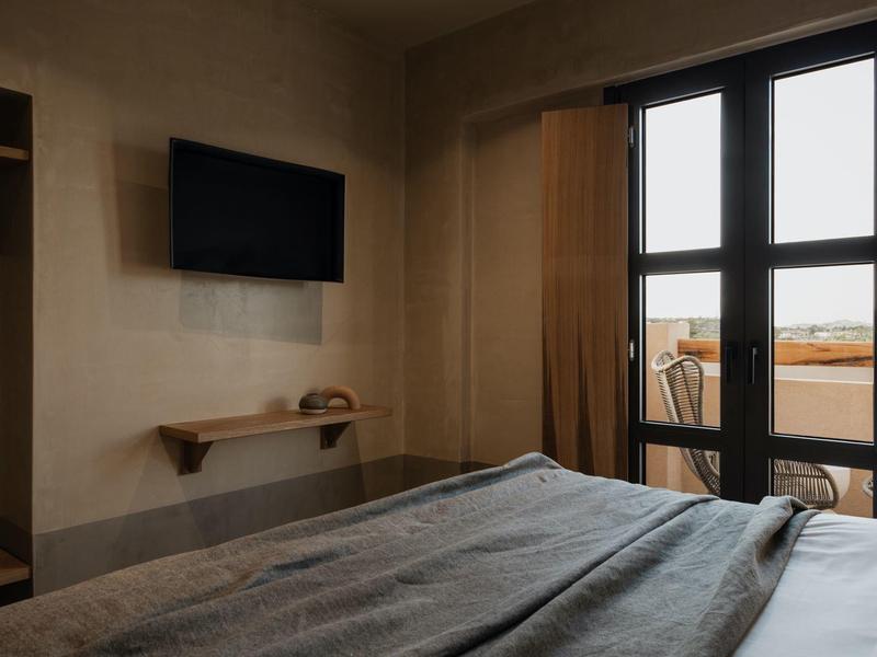 Hotelkamer met bed, aan de muur gemonteerde tv en balkon deur die natuurlijk licht binnenlaat.