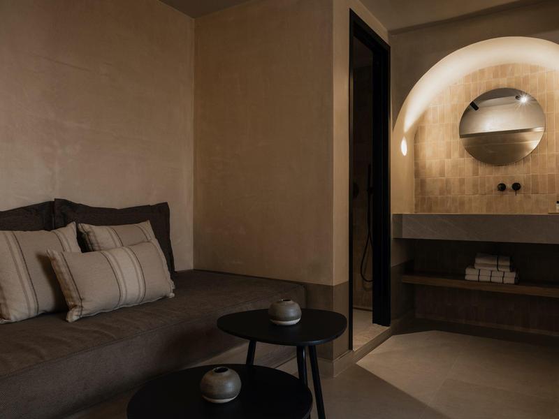 Gezellige hoek met bank, kussens en twee kleine tafels in warm verlichte kamer.