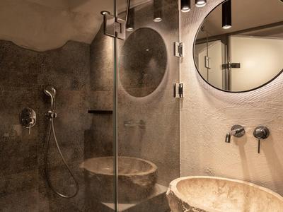 Salle de bain moderne avec lavabos en pierre naturelle et miroir rond sous lumière chaude.