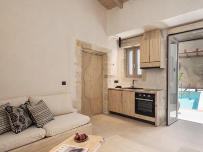 Petite cuisine avec armoires en bois, canapé et vue sur une piscine à travers une porte vitrée.