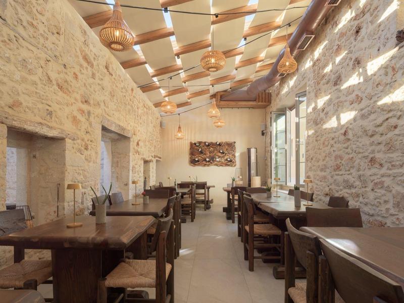 Salle à manger avec tables et chaises en bois dans une pièce lumineuse aux murs en pierre et plafond en bois.