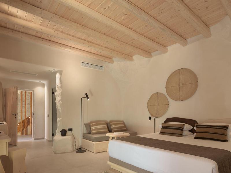 Chambre d'hôtel moderne avec lit double et coin salon, plafond à poutres claires et tons neutres.