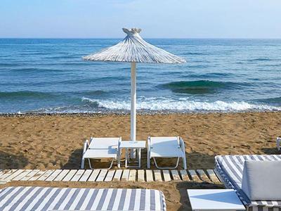 Nadmorski hotel z kilkoma budynkami, leżakami na plaży i morzem na pierwszym planie.