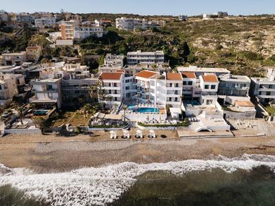 Hotel nadmorski z basenem i leżakami na plaży, otoczony apartamentami i wzgórzami.