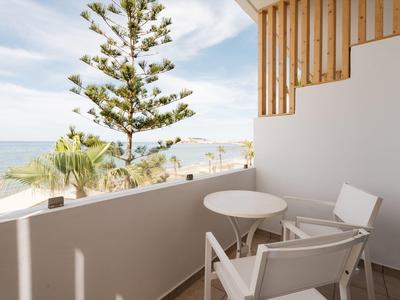 Balkon z dwoma krzesłami i stołem z widokiem na palmy i morze pod czystym niebem.