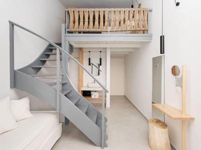 Jasne pomieszczenie z szarą spiralną klatką schodową, białą sofą i drewnianymi meblami.