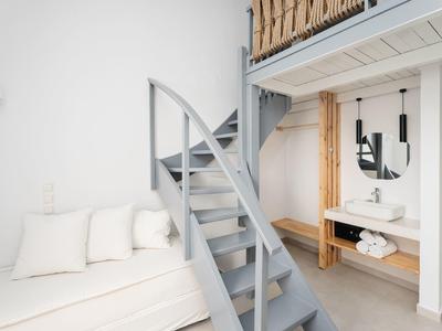 Jasny pokój z nowoczesną szarą spiralną klatką schodową, leżanką i drewnianymi detalami na lustrze i półce.