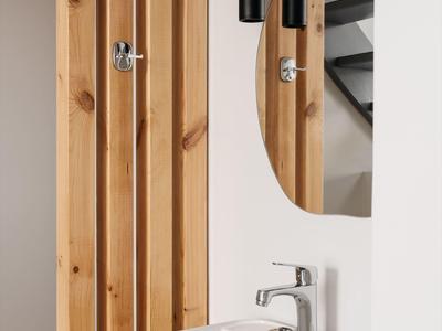 Nowoczesna łazienka z białą umywalką, drewnianymi panelami i owalnym lustrem na ścianie.