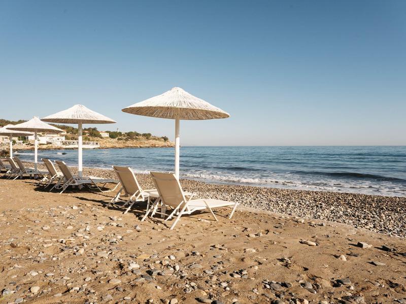 Puste leżaki z parasolami na spokojnej kamienistej plaży pod czystym niebem.