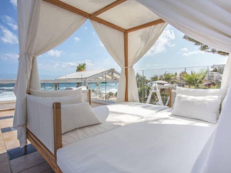 Białe łóżko dzienne z zasłonami na tarasie z widokiem na morze pod błękitnym niebem.